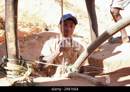 Ilakaka, Madagascar - 30 avril 2019: Inconnu homme malgache debout dans le sol mine de pierre précieuse trou ou puits, moitié corps visible, corde de maintien - abou Banque D'Images