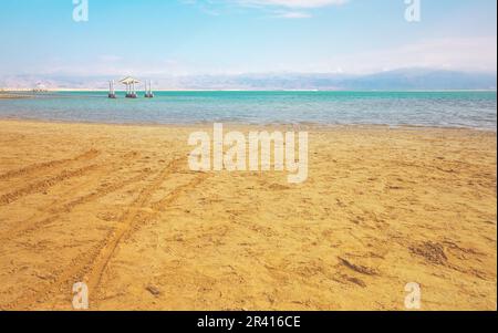 Journée calme à la plage de la mer Morte d'Ein Bokek, eau verte bleue, abri de soleil à proximité, le soleil brille sur la plage de sable Banque D'Images