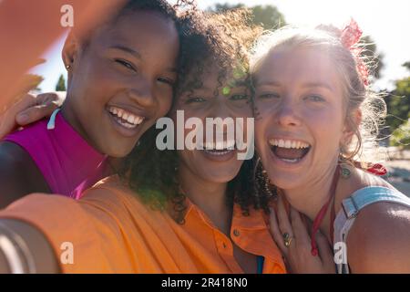 Portrait d'amis féminins variés et heureux embrassant et souriant à la plage, avec espace de copie Banque D'Images