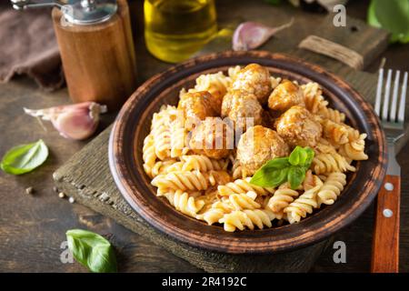 Cuisine italienne maison. Les pâtes italiennes fusilli ne contiennent pas de gluten et sont accompagnées de boulettes de viande dans une sauce tomate et de basilic sur une table rustique. Banque D'Images