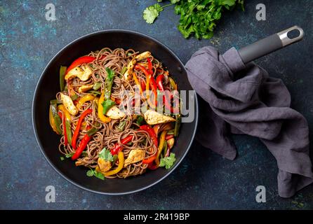 Plat japonais de nouilles soba de sarrasin avec poulet et légumes carottes, poivron et haricots verts au wok sur fond bleu foncé Banque D'Images