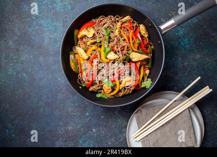 Plat japonais de nouilles soba de sarrasin avec poulet et légumes carottes, poivron et haricots verts au wok sur fond bleu foncé Banque D'Images