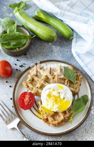 Le concept de petit déjeuner diététique et sain. Gaufres végétaliennes aux épinards et aux courgettes avec un œuf poché sur une table en pierre. Banque D'Images