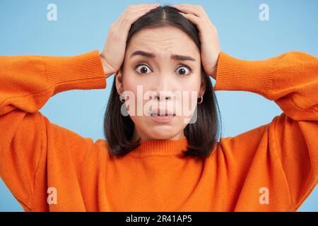 Gros plan de la femme asiatique choquée dans la panique, anxieux, semble terrifiée, se dresse sur fond bleu studio Banque D'Images
