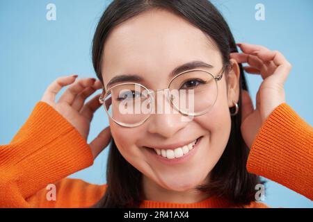 Gros plan portrait de la belle jeune femme asiatique en lunettes, souriant et regardant heureux, essayant de nouvelles lunettes à la boutique d'opticiens, s Banque D'Images