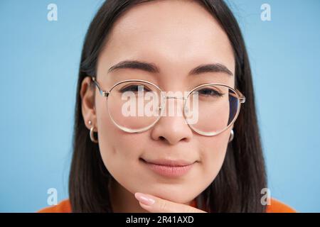 Gros plan d'une femme asiatique semble intriguée, porte des lunettes, s'accroupille, pense, prend ses suppositions, se tenir debout Banque D'Images