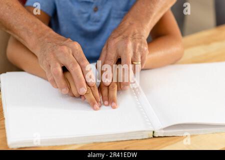 Des mains de grand-père caucasien aide le petit-fils aveugle à lire un livre en braille à la maison Banque D'Images