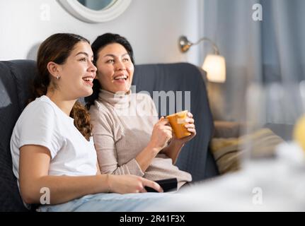 Deux amies qui regardent la télévision tout en étant assise sur un canapé à la maison Banque D'Images