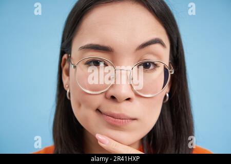 Gros plan d'une femme asiatique semble intriguée, porte des lunettes, s'accroupille, pense, prend ses suppositions, se tenir debout Banque D'Images