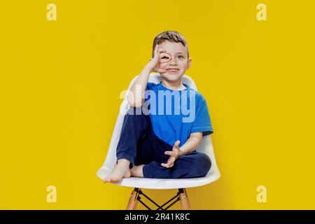 Joyeux petit garçon assis sur un fauteuil jaune - Portrait vif et ludique. Banque D'Images