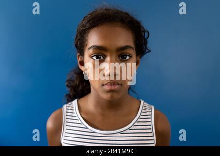 Portrait d'une jeune fille biraciale triste portant une robe rayée sur fond bleu avec espace de copie Banque D'Images