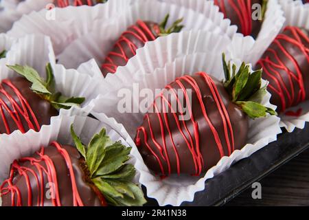 Plusieurs fraises enrobées de chocolat noir avec tuffs verts et bruine de glaçage rouge sur plateau noir Banque D'Images