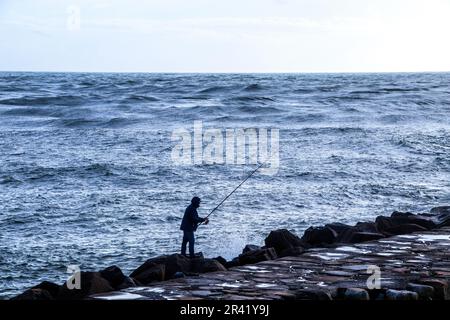 Pêcheur debout sur les rochers jetant une ligne dans l'océan Banque D'Images