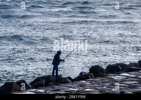 Pêcheur debout sur les rochers jetant une ligne dans l'océan Banque D'Images