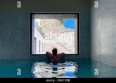 Femme se relaxant dans une piscine spa intérieure donnant sur une fenêtre, retraite de bien-être de luxe paisible, voyage et concept de détente Banque D'Images