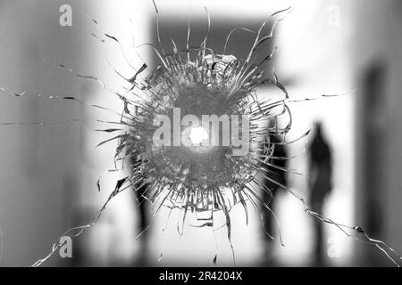 Trou de balle dans le verre avec des silhouettes en arrière-plan Banque D'Images