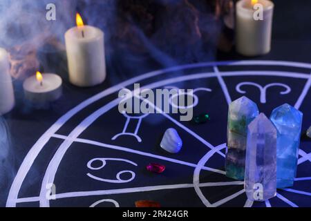 Pierres naturelles pour les signes du zodiaque, carte d'astrologie dessinée et bougies allumées sur table noire Banque D'Images
