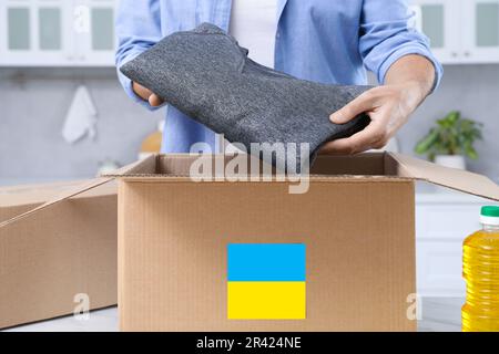 Aide humanitaire pour l'Ukraine. Homme mettant des vêtements dans une boîte de dons à la table blanche à l'intérieur, gros plan Banque D'Images