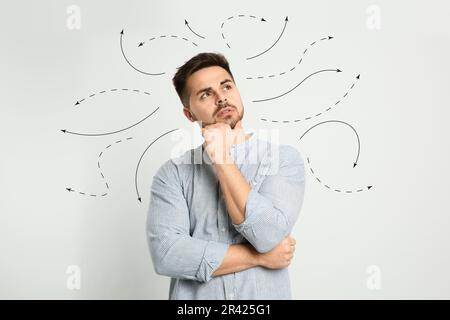 Choix dans la profession ou dans d'autres domaines de la vie, concept. Prise de décision, jeune homme réfléchi entouré de flèches dessinées sur fond gris clair Banque D'Images