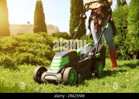 Femme coupant de l'herbe avec une tondeuse dans le jardin par temps ensoleillé, en gros plan Banque D'Images