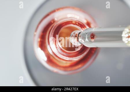 Bouteille d'huile ou de sérum et pipette dans une boîte de Petri sur fond gris. Produit cosmétique rose, concentration sélective Banque D'Images