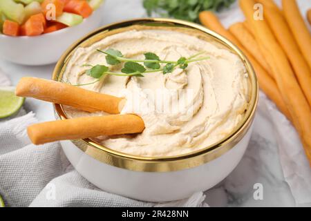 Délicieux houmous avec bâtonnets de grissini servis sur une table en marbre blanc, en gros plan Banque D'Images