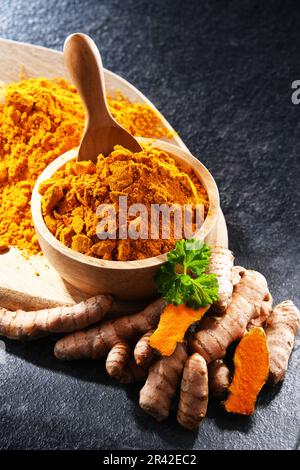 Composition avec un bol de curcuma moulu et son rhizome frais. Banque D'Images