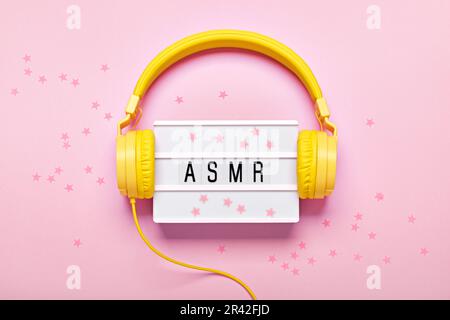 Casque jaune, visionneuse de lettres ASMR et confetti sur fond rose. Concept de sons anti-stress ASMR, pose plate Banque D'Images