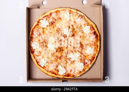 Pizza avec crevettes de fruits de mer et saumon dans une boîte d'emballage sur fond gris Banque D'Images