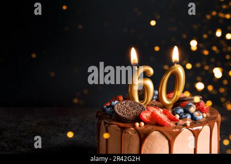 Gâteau d'anniversaire au chocolat avec baies, biscuits et bougies d'or numéro soixante sur fond noir, espace de copie Banque D'Images