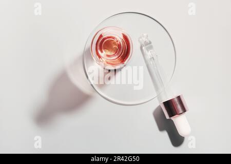 Bouteille d'huile ou de sérum et pipette dans une boîte de Petri sur fond gris. Produit cosmétique rose Banque D'Images