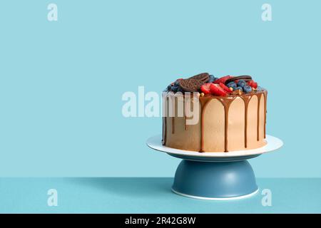 Gâteau d'anniversaire au chocolat avec baies et biscuits sur fond de table mural bleu, espace de copie Banque D'Images