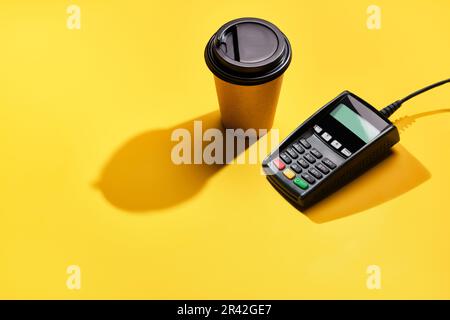 Terminal de paiement POS et café sur fond jaune. Concept de service financier minimal. Ombres à la mode, espace de copie Banque D'Images