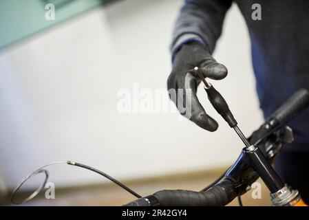 Entretien d'un vélo : homme méconnaissable utilisant des gants de protection pour démonter un vélo avec une clé Allen hexagonale dans son atelier de réparation. Banque D'Images