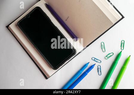 Conception à plat de bureau de travail avec papeterie colorée et outils d'écriture tels que stylos d'esquisse, mobile, trombones, stylo, et livre, sur un bureau blanc Banque D'Images