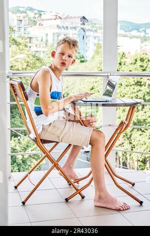 Préadolescent avec l'expression curieuse et intéressée demande au sujet de la vidéo sur ordinateur portable. Blonde garçon aime passer des vacances d'été au bord de la mer Banque D'Images