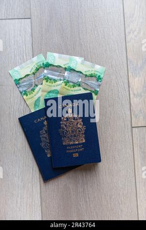 Poser des passeports canadiens à plat avec de l'argent canadien sur un fond en bois neutre Banque D'Images