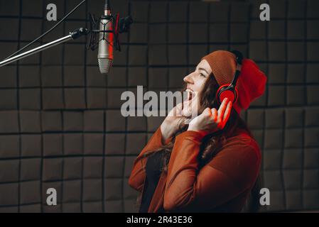 Une jeune femme dans un casque chante émotionnellement dans le microphone du studio d'enregistrement sonore. Star, talent, préparation du spectacle, enregistrement en studio. Insonorisation Banque D'Images