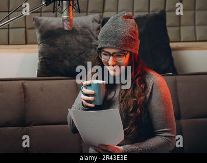 Une femme boit du thé chaud ou du café dans un confortable studio d'enregistrement sonore le matin avant de diffuser des émissions en direct. Belle artiste vocale féminine appréciant Banque D'Images