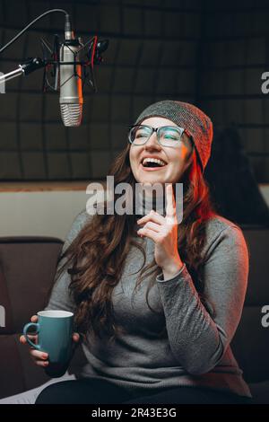 Une femme boit du thé chaud ou du café dans un confortable studio d'enregistrement sonore le matin avant de diffuser des émissions en direct. Belle artiste vocale féminine appréciant Banque D'Images