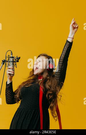 La chanteuse positive de brunette ayant plaisir chante la chanson. Gros plan d'une jeune artiste pop caucasienne dans des écouteurs souriant pendant la représentation Banque D'Images