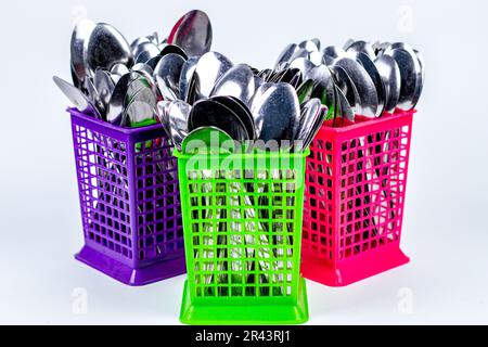 pile de cuillères en métal dans des paniers en plastique colorés isolés sur fond blanc Banque D'Images