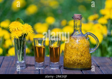 Décoration faite maison de fleurs de pissenlit en deux verres et en bouteille de verre sur une table en bois dans un jardin d'été, gros plan Banque D'Images