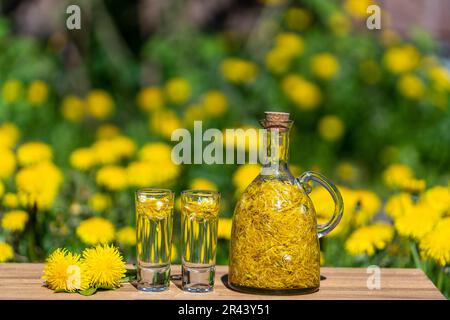 Décoration faite maison de fleurs de pissenlit en deux verres et en bouteille de verre sur une table en bois dans un jardin d'été, gros plan Banque D'Images