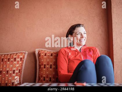 Une femme souriante se détend sur un canapé à côté d'un mur en adobe au Maroc Banque D'Images