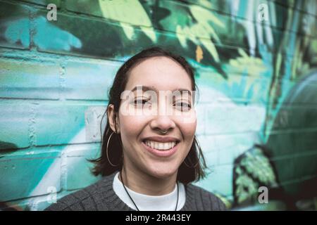 Jeune femme avec un sourire crasseux debout à côté du mur de graffiti coloré Banque D'Images