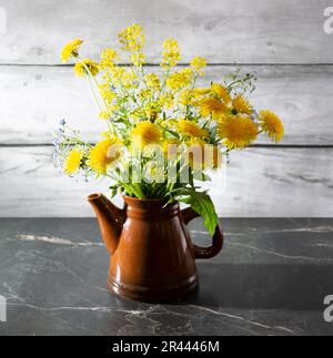 Encore la vie avec des pissenlits jaunes dans une théière sur une table en marbre foncé. Le concept est la vie vivante. Banque D'Images