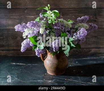 Encore la vie avec les lilas et la cerise d'oiseau blanc dans un vieux vase en argile sur une table en marbre foncé. Concept arôme de la vie. Banque D'Images