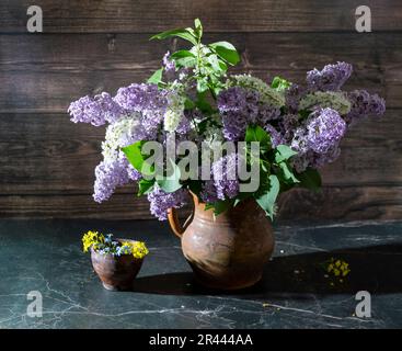 Encore la vie avec les lilas et la cerise d'oiseau blanc dans un vieux vase en argile sur une table en marbre foncé. Concept arôme de la vie. Banque D'Images