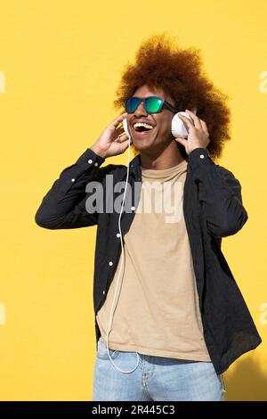 Joyeux jeune homme portant des lunettes de soleil et des écouteurs s'amusant Banque D'Images
